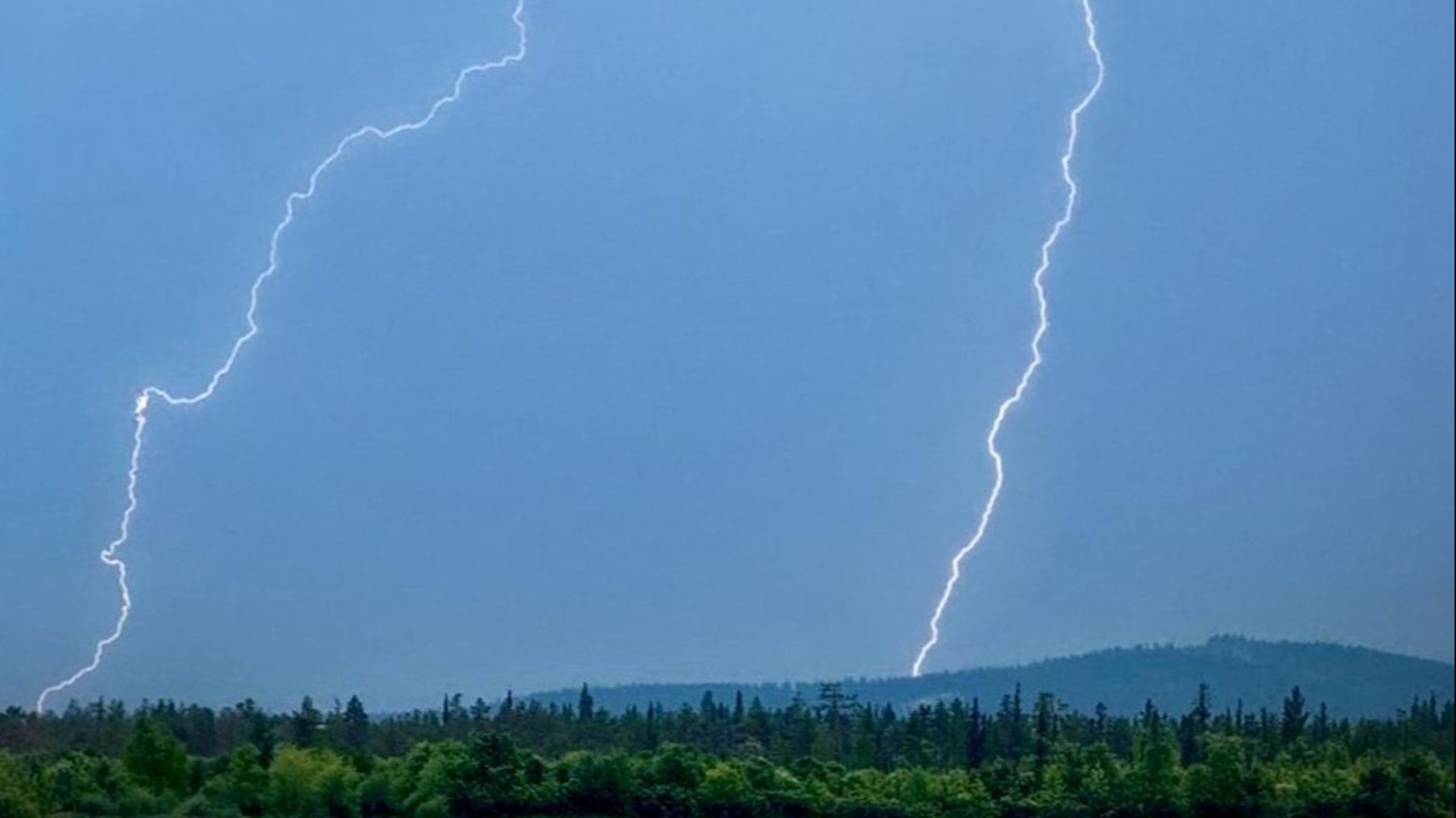 Ukkosrintamasta iskeneet kaksi maasalamaa. Etualalla metsää ja taustalla tunturimaisema. 