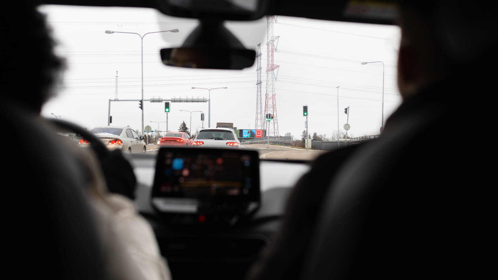 Nainen ja mies ajavat autoa. Auton etuosassa navigaattori on päällä, ikkunasta näkyy risteys liikennevaloineen.