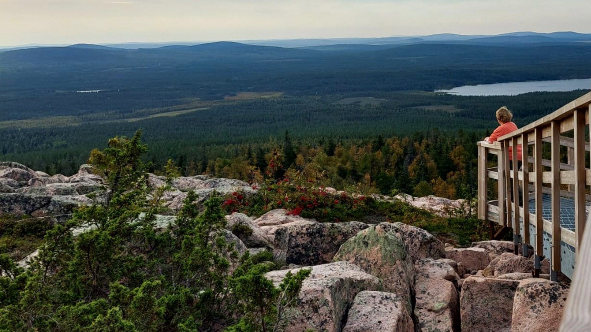 Naishenkilö nojaa retkeilyreitin portaiden kaiteeseen. Taustalla siintää tunturi maisema. Etualalla erottuu rakkakivikko.