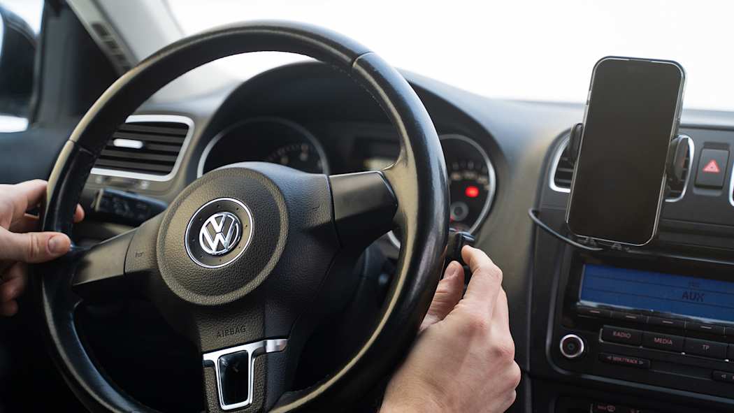 Henkilö ajaa autoa. Puhelin on asetettu puhelintelineeseen.