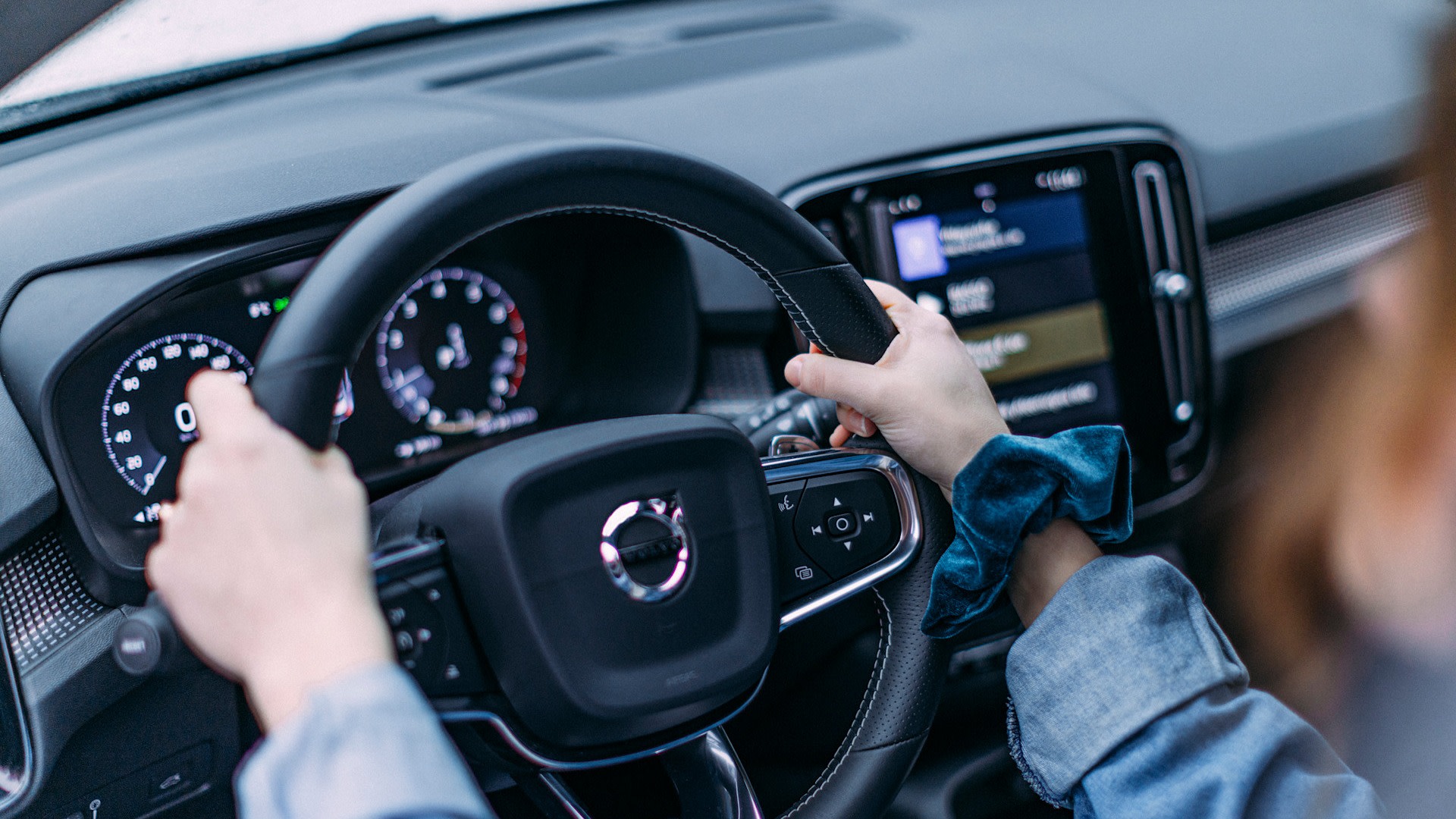 Henkilö ajaa autoa. Puhelin on asetettu puhelintelineeseen.