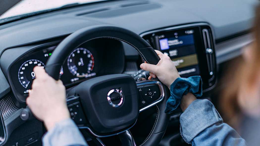 Henkilö ajaa autoa. Puhelin on asetettu puhelintelineeseen.