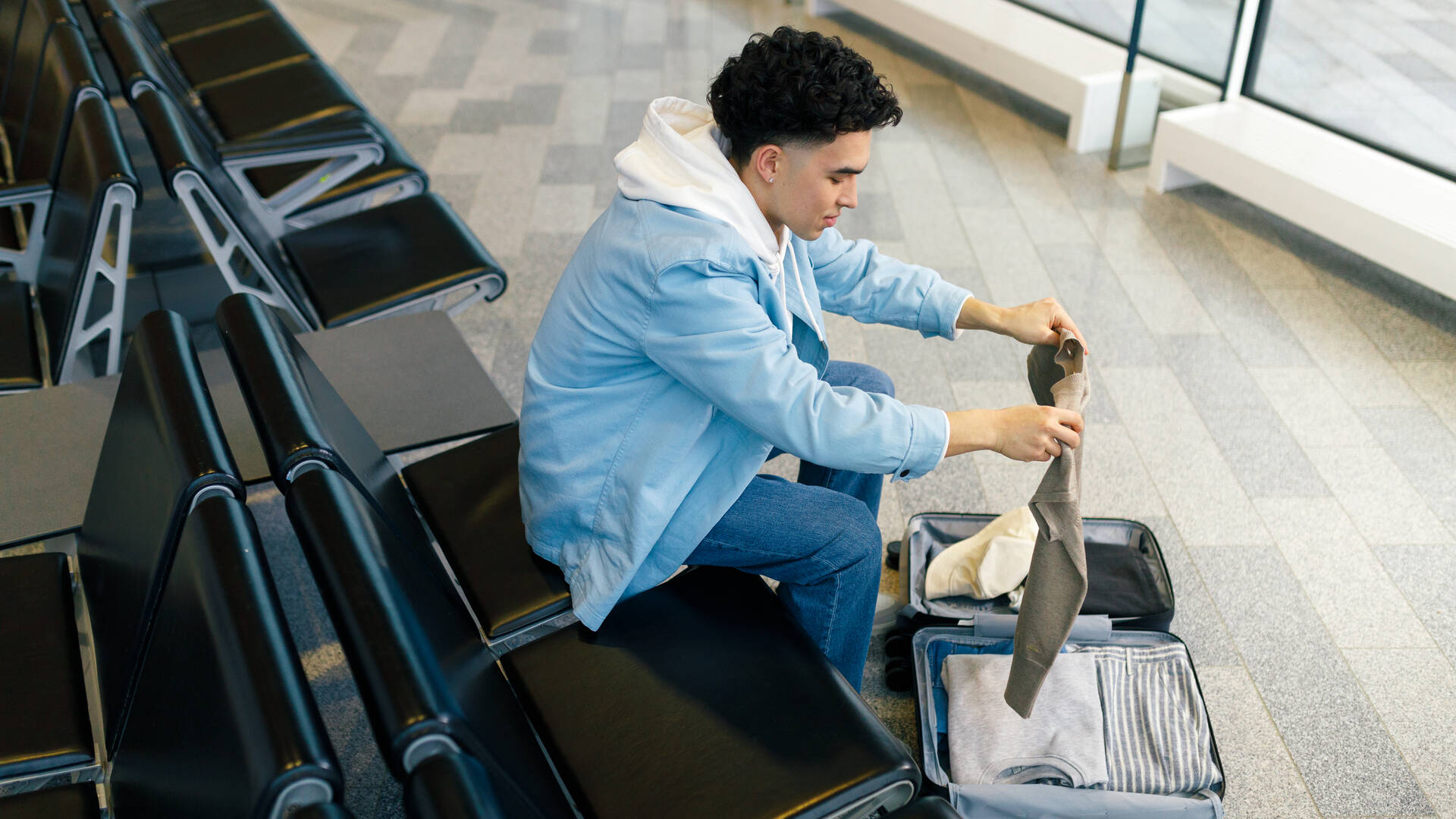 Nuori mies viikkaa vaatetta matkalaukkuunsa lentokentällä.