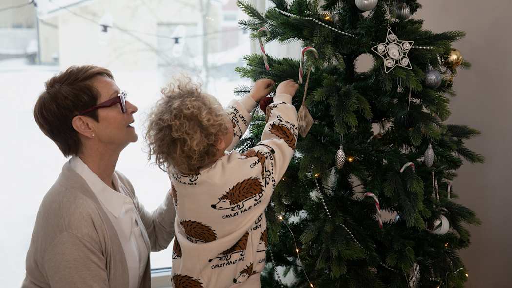 Ett barn dekorerar julgranen med sin mormor.