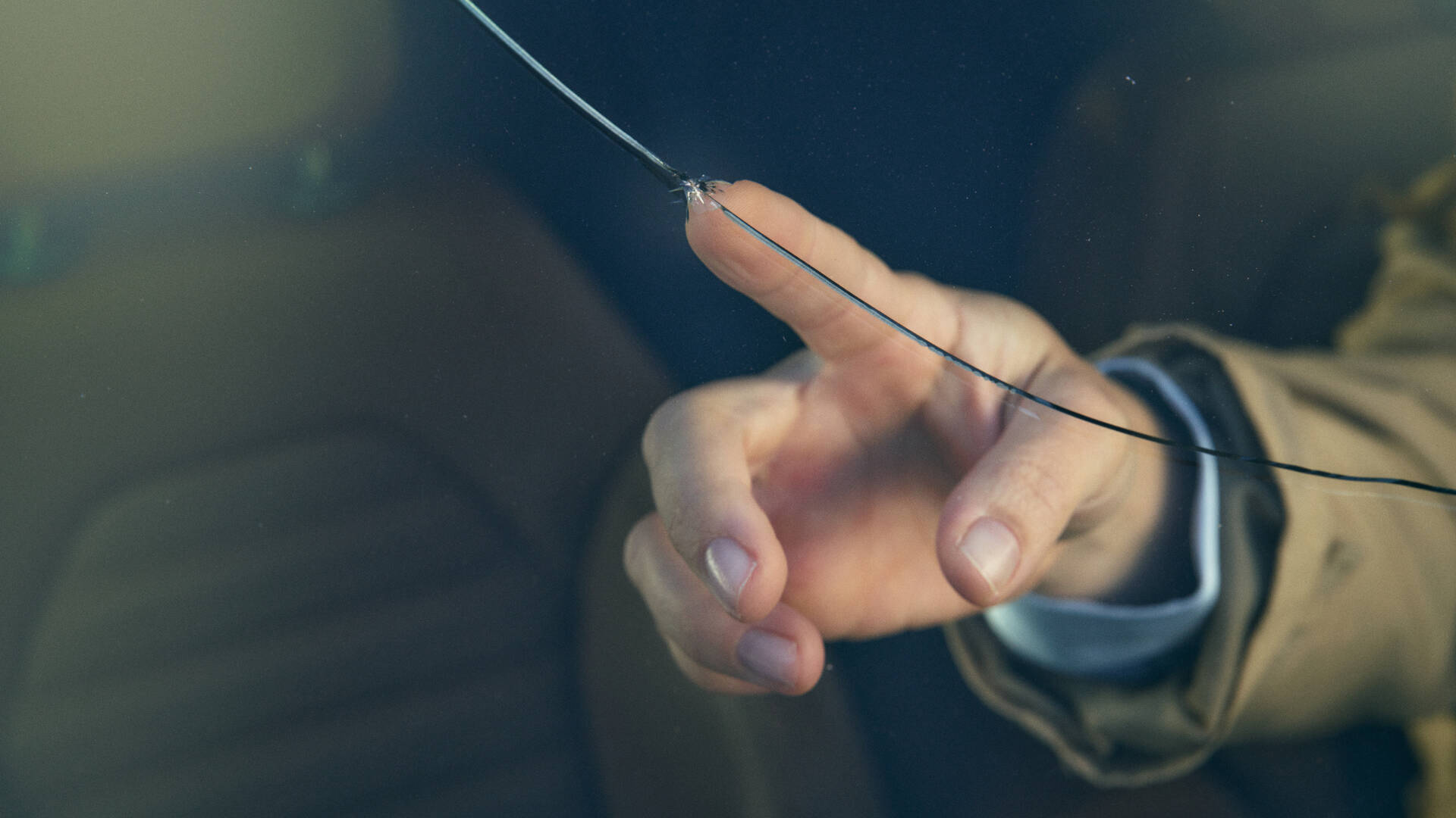 Ihminen koskee sormella kiveniskemää auton tuulilasissa.