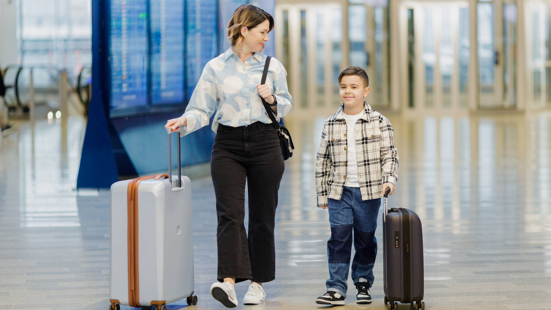 Äiti ja poika kävelevät lentokentällä matkalaukkujen kanssa.