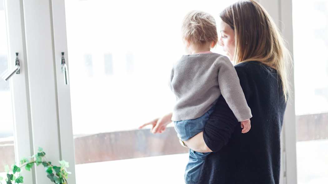 Nainen pitää lasta sylissään ja katsoo ikkunasta.