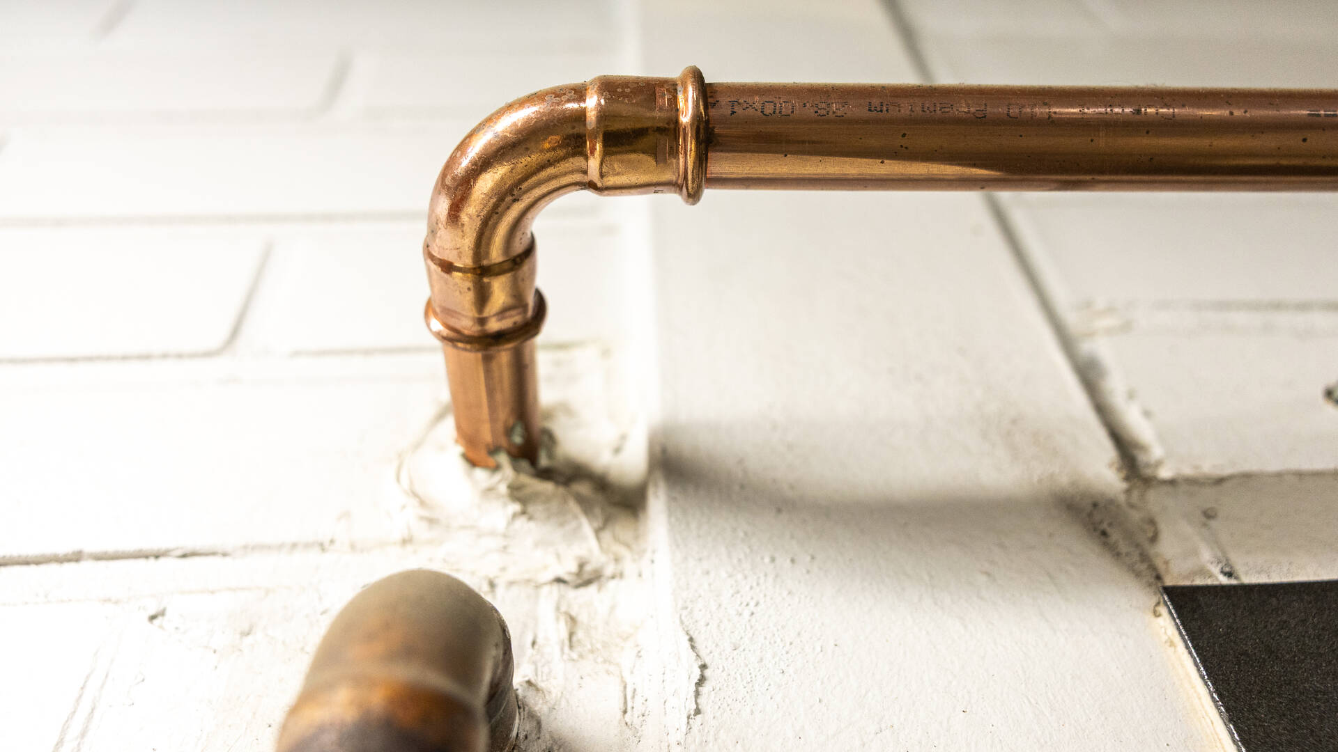 Kuparinvärinen vesiputki kaartuu ulos seinästä.