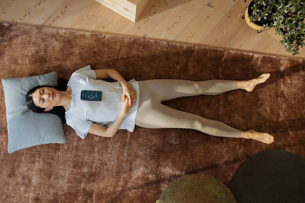 Nainen makaa matolla pää tyynyllä silmät kiinni rinnallaan puhelin, joka mittaa sydämen toimintaa.