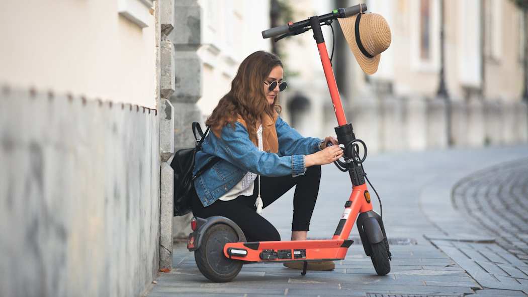 Nainen on kumartunut ottamaan sähköpotkulautaa käyttöön kaupungin kadulla.