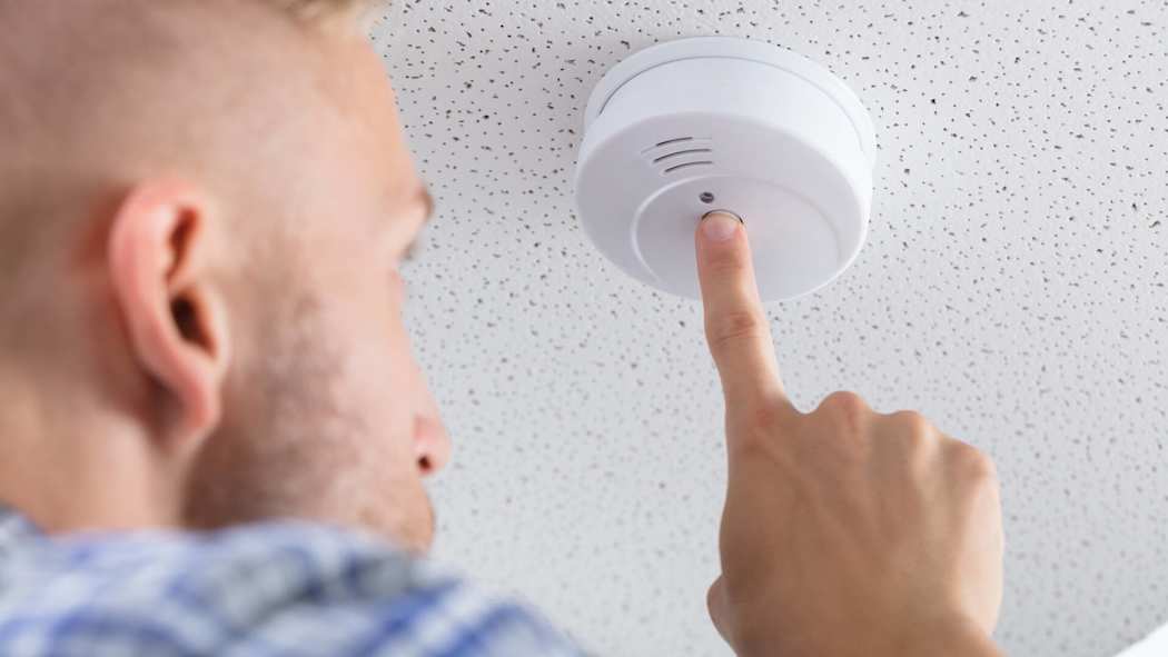 Mies painaa katossa olevan palovaroittimen testinappia.