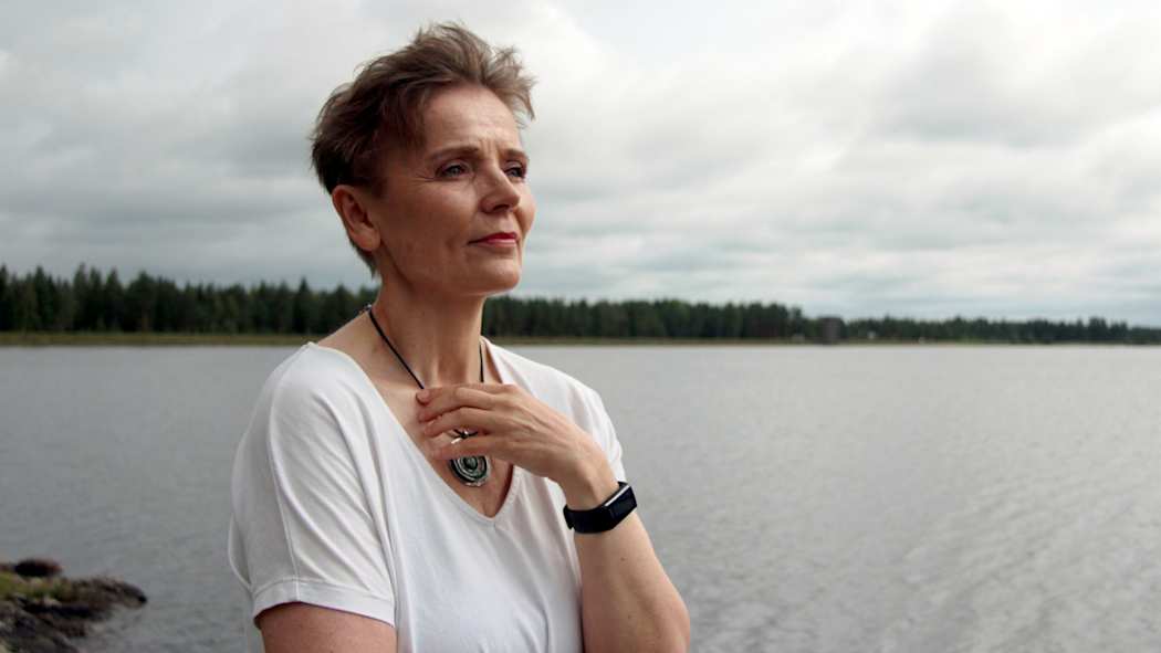 Tarja Hoppi katsoo kaukaisuuteen järven rannalla.