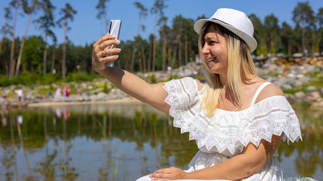 Nainen ottaa puhelimellaan selfietä järven rannalla.