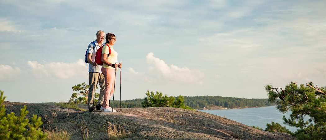 Ulkoileva eläkeläispariskunta kävelysauvojen kanssa kallion laella.