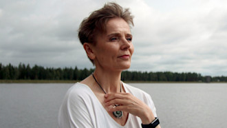 Valkopuseroinen nainen mietteliäänä, järvi taustalla.