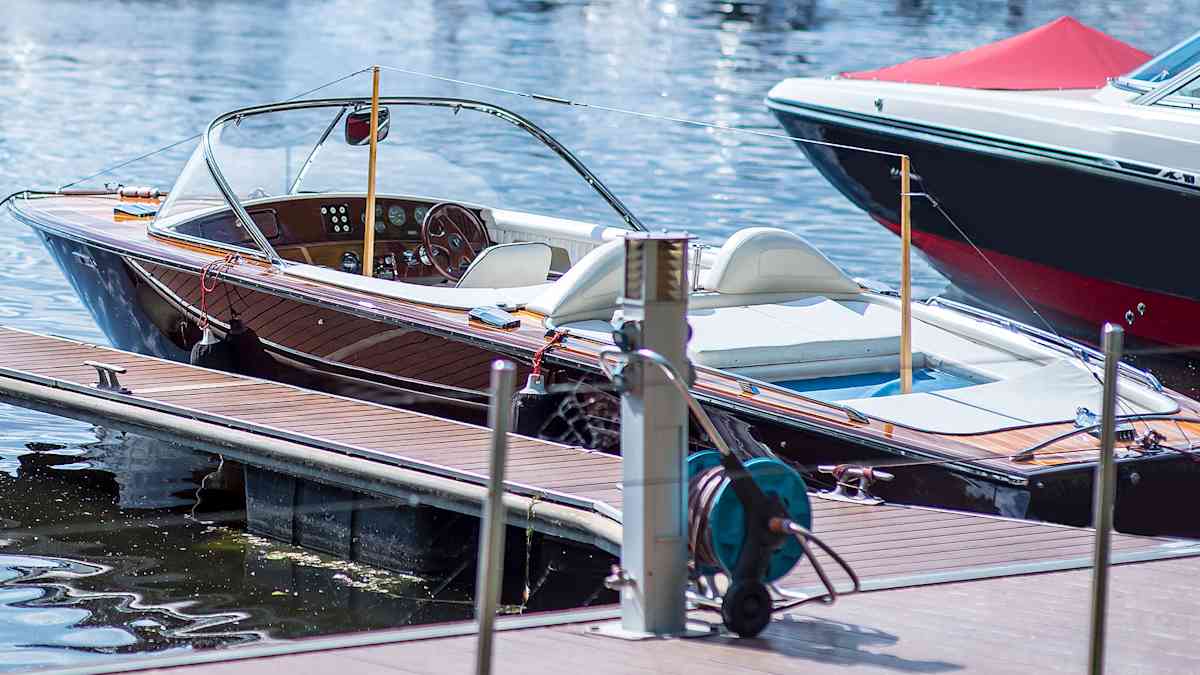 Klassinen, puurunkoinen moottorivene on kiinnitettynä puiseen laituriin aurinkoisessa venesatamassa.