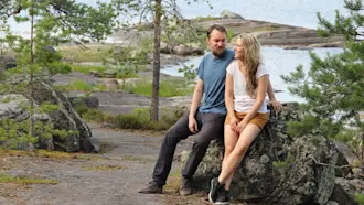 Mies ja nainen nojaavat isoon kivenlohkareeseen veden rannalla