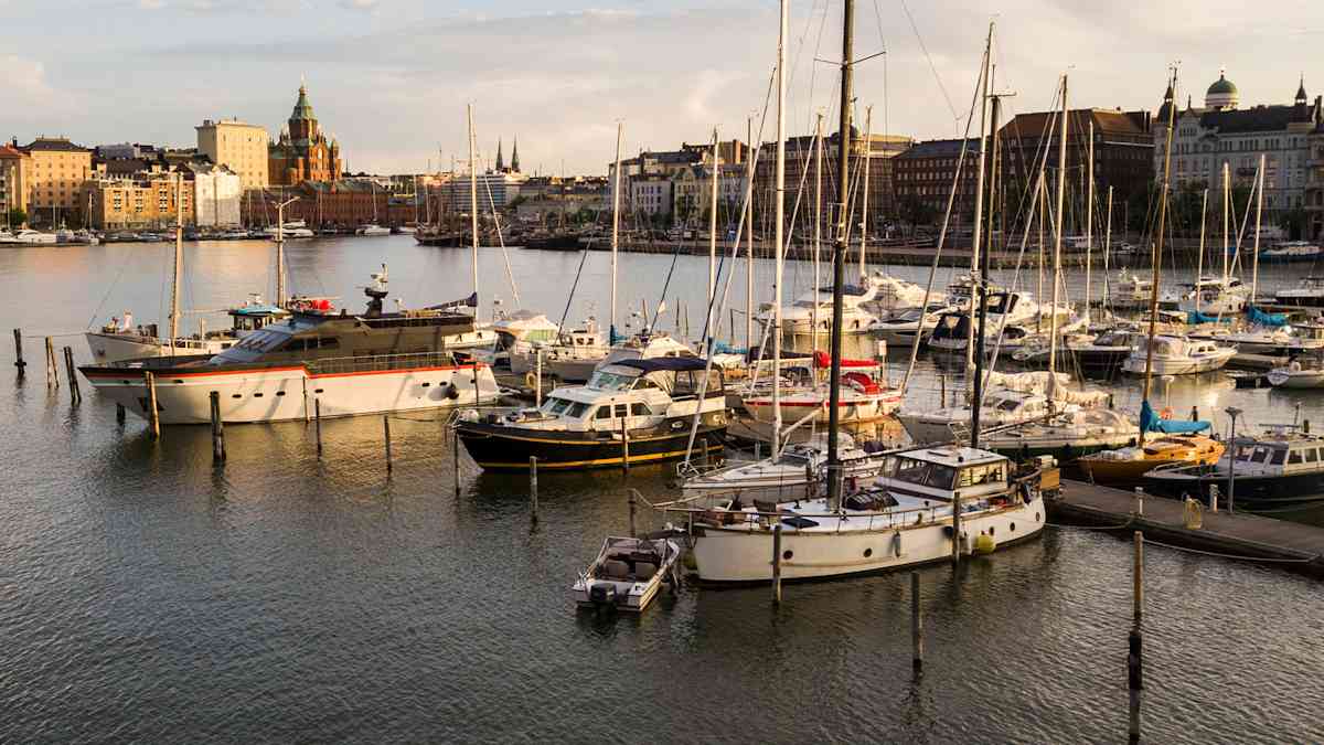 Venesatama, jossa on purjeveneitä ja moottoriveneitä laitureihin kiinnitettyinä ilta-auringon valossa.